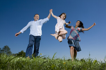 Junge Familie mit Tochter (6-7) bei einem Spaziergang über eine Wiese, die Spaß macht - CLF00563