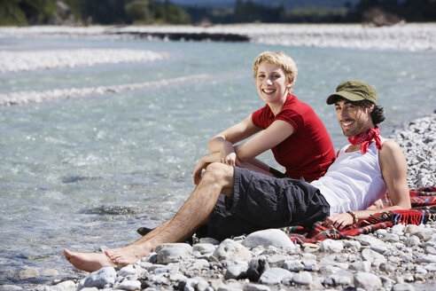 Deutschland, Bayern, Tölzer Land, Junges Paar sitzt am Flussufer - WESTF09955