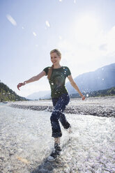 Deutschland, Bayern, Tölzer Land, Junge Frau läuft lächelnd durch Fluss - WESTF09912