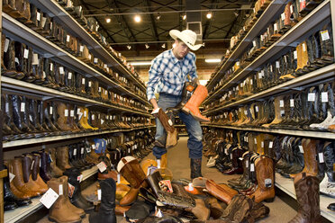 USA, Texas, Dallas, Junger Mann sucht Cowboystiefel in einem Schuhgeschäft aus - PK00244