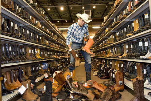USA, Texas, Dallas, Young man choosing cowboy boots in shoe store - PK00244
