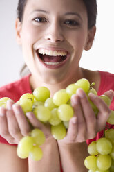Young woman holding bunch of grapes, laughing - MAEF01277