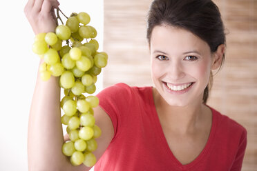 Junge Frau hält lächelnd eine Weintraube - MAEF01276