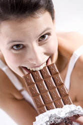 Young woman biting into chocolate bar, smiling - MAEF01263