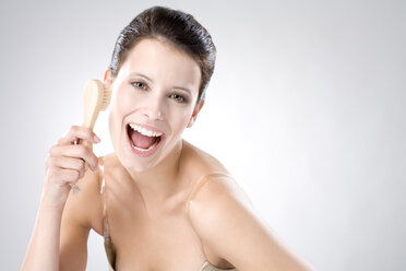 Young woman using peeling brush, laughing, close up - MAEF01258