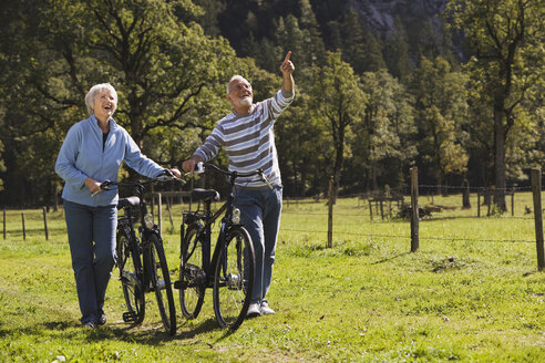 Austria, Karwendel, Senior couple pushing bikes across path - WESTF10533