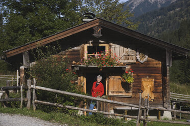 Austria, Karwendel, Senior woman standing in front of log cabin, smiling - WESTF10505