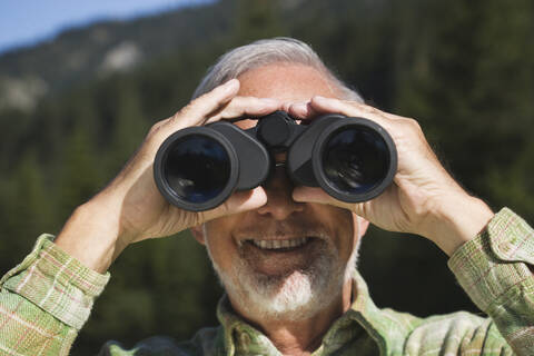 Österreich, Karwendel, Älterer Mann schaut durch ein Fernglas, Porträt, lizenzfreies Stockfoto