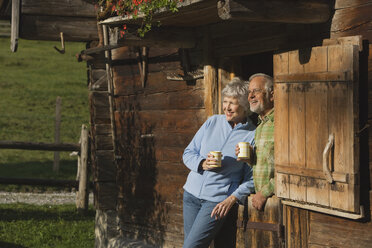 Austria, Karwedel, Senior couple leaning on log cabin, holding mugs - WESTF10467