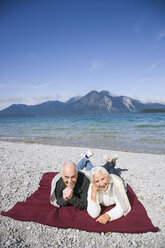Germany, Bavaria, Walchensee, Senior couple relaxing on lakeshore - WESTF10146