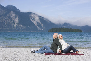 Germany, Bavaria, Senior couple relaxing on lakeshore, sitting back to back - WESTF10143