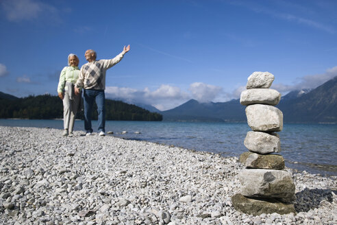 Germany, Bavaria, Walchensee, Senior couple taking a walk, stone pyramid in foreground - WESTF10125