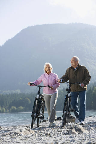 Germany, Bavaria, Walchensee, Senior couple pushing bikes across lakeshore stock photo