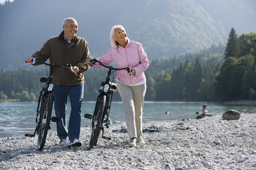 Germany, Bavaria, Walchensee, Senior couple pushing bikes across lakeshore - WESTF10108