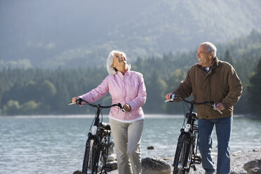 Germany, Bavaria, Walchensee, Senior couple pushing bikes across lakeshore - WESTF10107