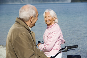 Germany, Bavaria, Walchensee, Senior couple pushing bikes across lakeshore - WESTF10106