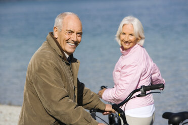 Germany, Bavaria, Walchensee, Senior couple pushing bikes across lakeshore - WESTF10105