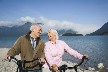 Germany, Bavaria, Walchensee, Senior couple pushing bikes across lakeshore - WESTF10104