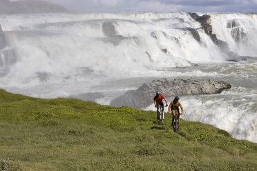 Island, Männer beim Mountainbiking, Wasserfall im Hintergrund - FF00987