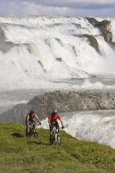 Island, Männer beim Mountainbiking, Wasserfall im Hintergrund - FF00986