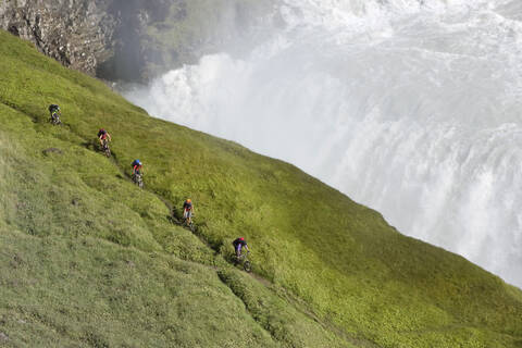 Island, Männer beim Mountainbiking neben einem Wasserfall, lizenzfreies Stockfoto