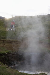 Island, Mountainbiker mit Blick auf eine heiße Quelle - FF00977