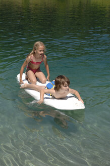 Boy and girl (6-7) on surfboard floating on water - CRF01660