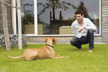 Junger Mann spielt mit Hund im Garten - NHF01021