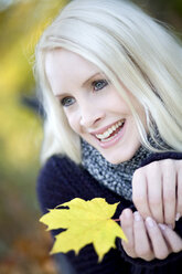 Young woman holding maple leaf, laughing, portrait - MAEF01472