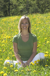 Austria, Salzburger Land, Young woman sitting in meadow, smiling - HHF02796