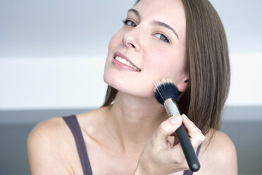 Young woman using make-up brush, portrait, close up - WESTF10911