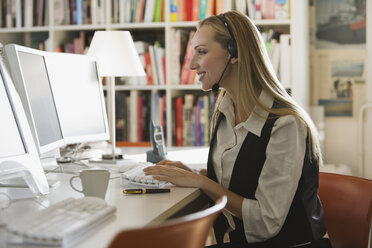 Young woman in office with headset using computer, portrait - WESTF10703