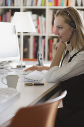 Young woman in office with headset using computer, portrait - WESTF10702