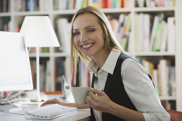 Junge Frau im Büro, die eine Tasse Kaffee hält, lächelnd, Porträt - WESTF10681