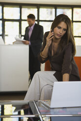 Young woman in office using mobile phone, man in background - WESTF10680