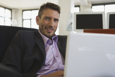 Business man in office using laptop, portrait - WESTF10675