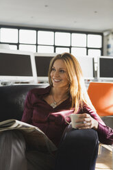 Geschäftsfrau im Büro mit Tasse und Zeitung, lächelnd, Porträt - WESTF10584