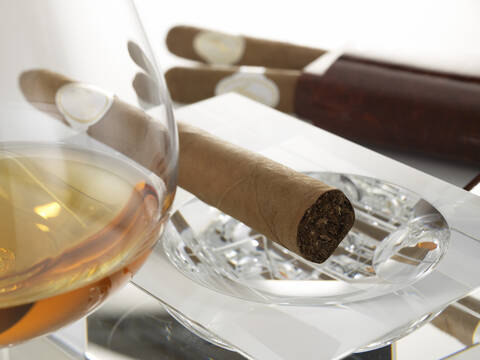 Cigar in ashtray with glass of cognac, close-up stock photo