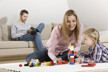 Vater liest Buch, Mutter und Tochter spielen im Vordergrund - CLF00649