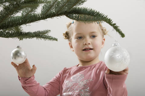 Kleines Mädchen (3-4) betrachtet eine Weihnachtskugel, lizenzfreies Stockfoto