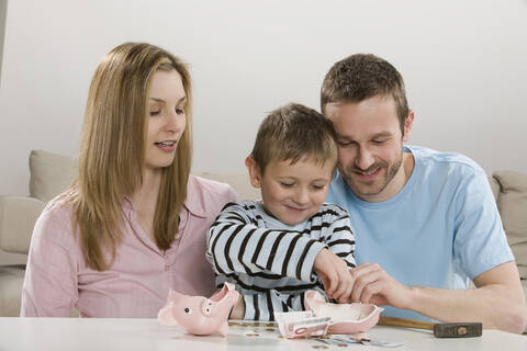 Eltern und Sohn (4-5) betrachten ein zerbrochenes Sparschwein und zählen das Geld, lizenzfreies Stockfoto