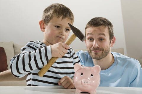 Vater und Sohn (4-5) betrachten ein Sparschwein, der Junge hält einen Hammer, lizenzfreies Stockfoto