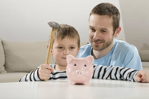 Vater und Sohn (4-5) betrachten ein Sparschwein, der Junge hält einen Hammer, lizenzfreies Stockfoto