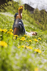 Junger Mann entspannt sich auf einer Wiese, Löwenzahnblüten zwischen den Zehen - WWF00421