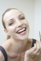 Young woman holding lip brush, laughing, portrait, close-up - WESTF10819