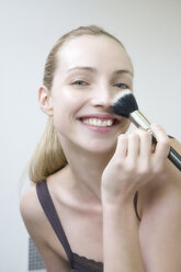 Young woman using make-up brush, smiling, portrait, close-up - WESTF10809