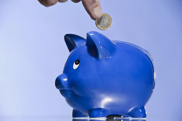 Person putting Euro coin into piggy bank - CLF00697