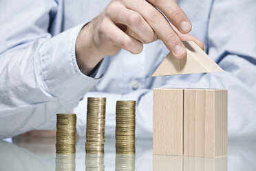 Person building house with building bricks beside stack of coins, close up - CLF00695