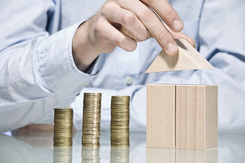 Person building house with building bricks beside stack of coins, close up - CLF00695