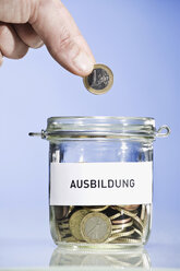 Person putting Euro coin into preserving jar, close up - CLF00682